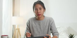 年轻的亚洲女商人使用电脑笔记本电脑与同事在视频电话会议的计划，而工作在家在卧室。