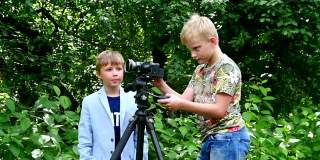 小男孩们带着摄像机拍摄关于自然绿地背景的影片。
