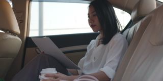 亚洲女商人在时尚的办公室服装工作和喝一次性纸杯热饮在都市现代城市的汽车后座的早晨。