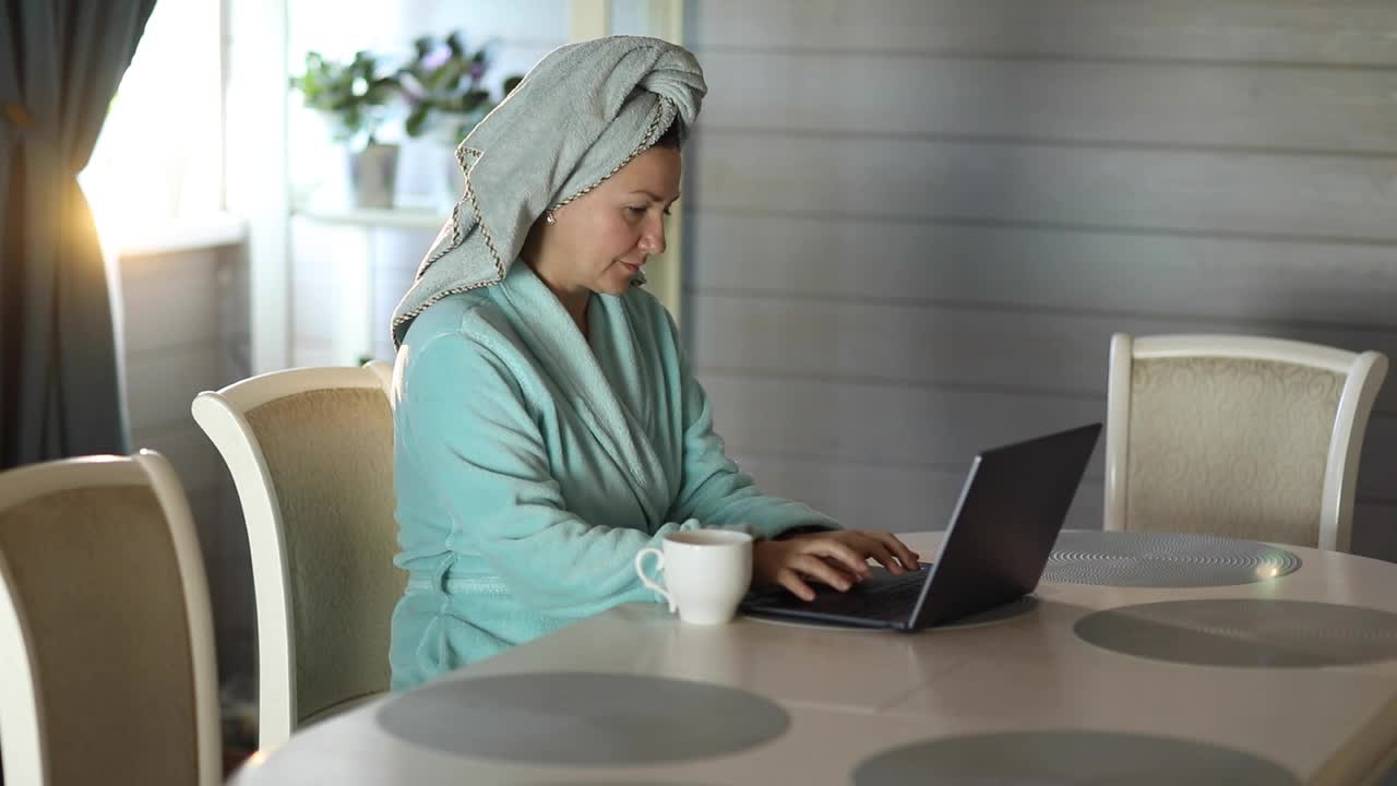 一位女士淋浴后喝咖啡，用笔记本电脑工作