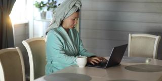 一位女士淋浴后喝咖啡，用笔记本电脑工作
