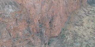 摄像机沿着侵蚀模式的红棕色悬崖向下拍摄到干燥的岩石景观中的水坑，水是停滞的和绿色的。航拍视频