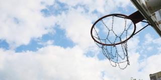 篮球场上的篮筐和篮球的侧视图。背景是天空和云彩