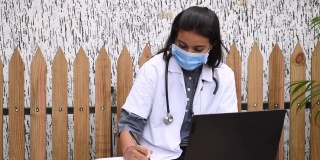 女医生坐在医院的桌子上用笔记本电脑开处方。医生在诊所戴口罩