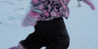 冬天，假期，游戏，家庭概念-慢动作接近婴儿走过深雪。孩子们的脚踩在雪道上。学前班的小孩穿着黑色的连体衣在寒冷的季节下雪