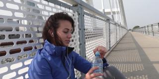 年轻美丽的健身运动慢跑的女人蹲在桥上休息喝水补水后有氧运动和训练健康的生活通过户外跑步