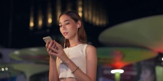 年轻亚洲女人的4K肖像走在城市的街道听音乐从耳机在晚上