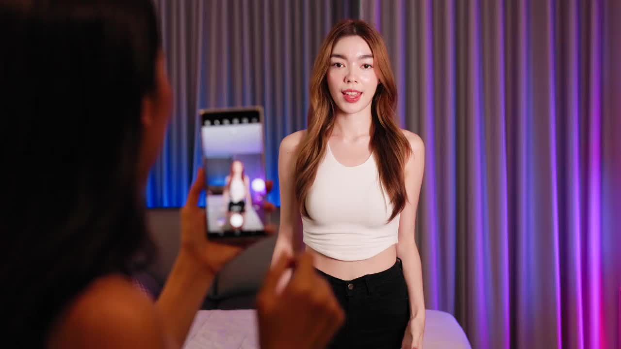 亚洲混血女性网红在手机社交媒体上拍摄舞蹈视频，在家玩乐。分享视频到社交媒体应用程序。