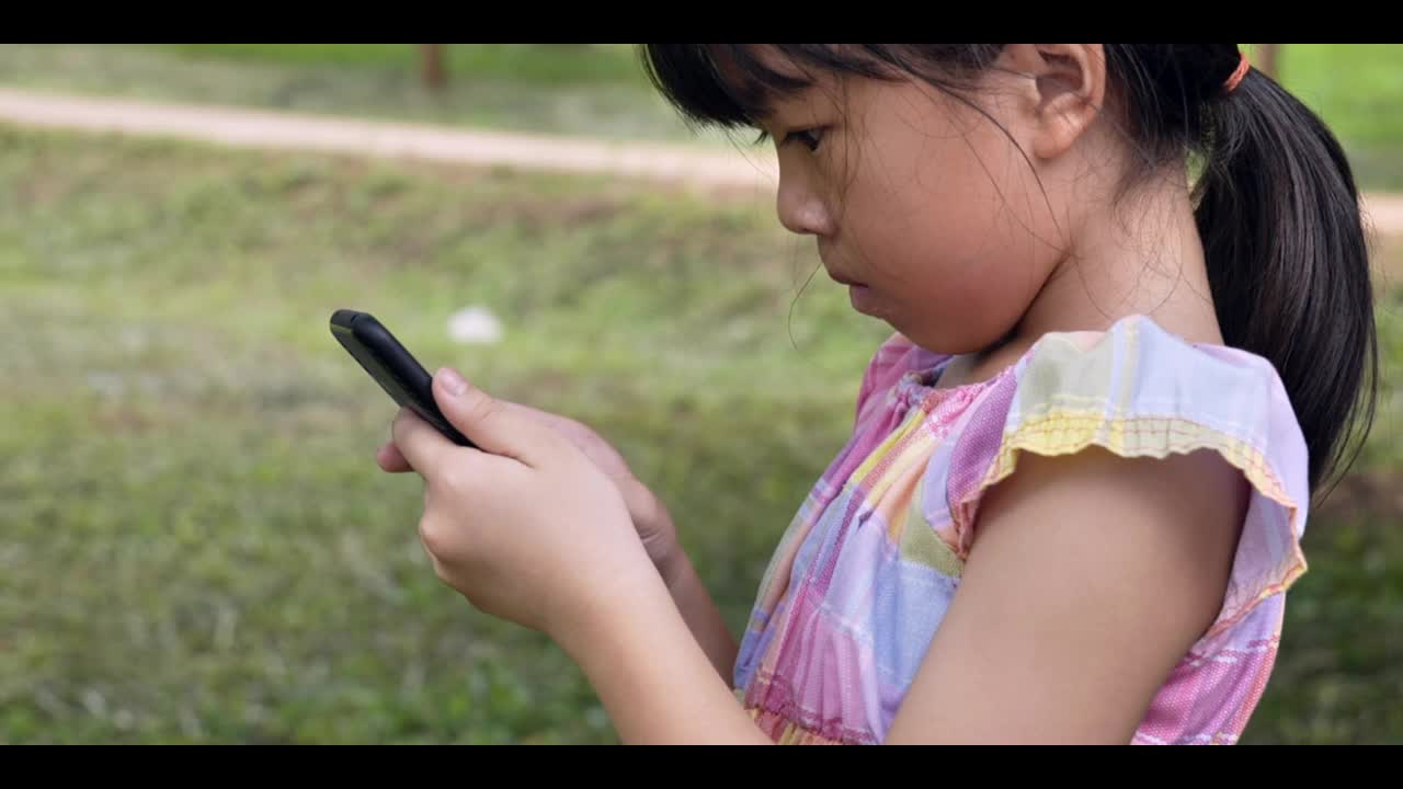 亚洲女孩在绿色公园的户外看智能手机。4k镜头慢动作