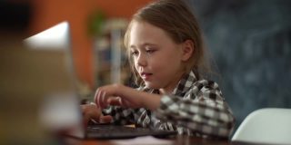 温馨客厅里，快乐的小女孩坐在书桌前，用笔记本电脑键盘打字。
