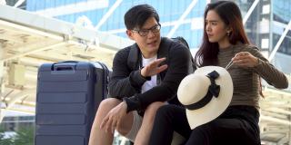 年轻的亚洲夫妇旅行者和行李坐在城市交谈。情人旅游者在假期外出旅游。