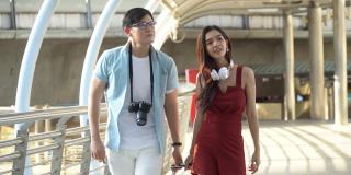 年轻的亚洲夫妇旅行者在步行和观光城市交谈行李。情人旅游者在假期外出旅游。