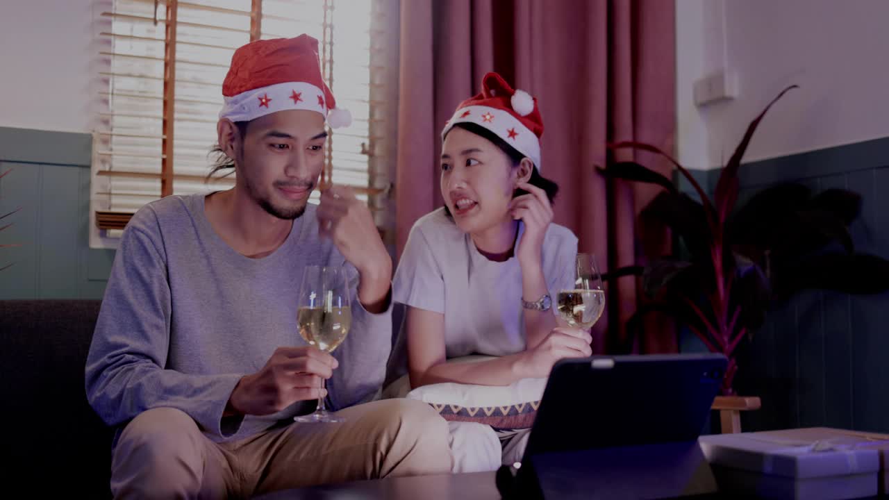 家庭年轻的亚洲夫妇坐在一起庆祝。在圣诞节与朋友视频通话，并在家里祝新年快乐。喝香槟，在平板电脑上在线看电影。通信技术