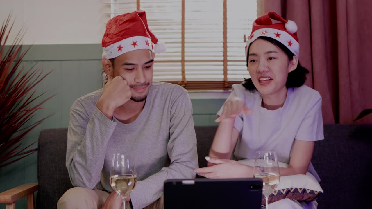 家庭年轻的亚洲夫妇坐在一起庆祝。在圣诞节与朋友视频通话，并在家里祝新年快乐。喝香槟，在平板电脑上在线看电影。通信技术