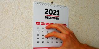 一名男子用手撕下挂在墙上的2021年日历的12月页，然后撕下2022年新日历的1月页
