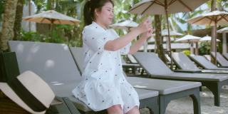 亚洲女性旅行者穿着休闲布衣享受假期日落时刻手用智能手机设备社交媒体交流。亚洲女性喜欢周末在海滩日落时间旅行。