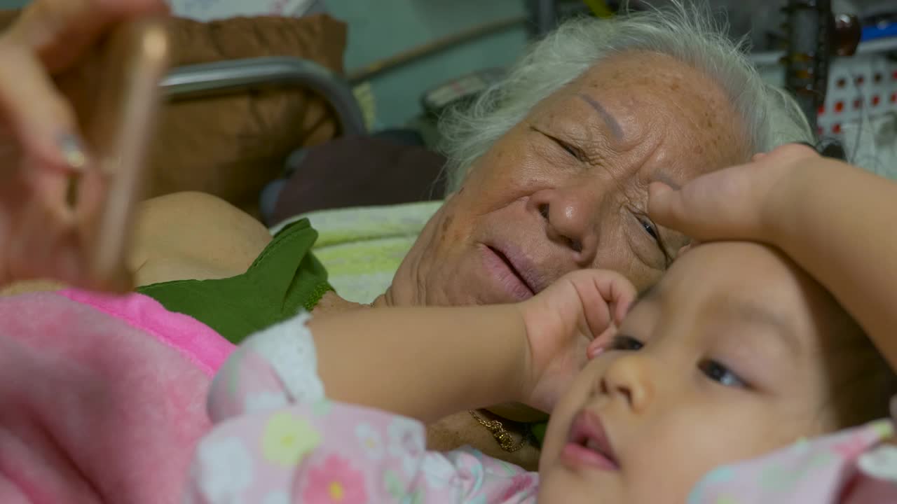 快乐的亚洲祖母和孙女有乐趣在床上聊天。