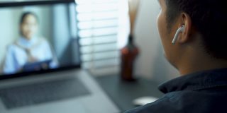 一名亚洲男子在家庭办公室用笔记本电脑与客户视频通话。