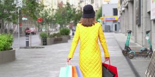优雅的购物女在购物后走在城市的街道上。