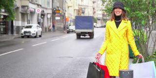 在购物中心附近的大街上，一个带着购物袋的快乐时尚女人正试图拦一辆出租车。快乐的生活方式和假日折扣的概念。