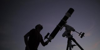 一个人的剪影，望远镜和夜空。业余天文学的概念。