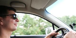 一名戴着深色太阳镜的男司机把双手放在方向盘上。在高速公路上开车，旅行