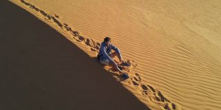 一名男子坐在沙漠中的沙丘上的航拍照片