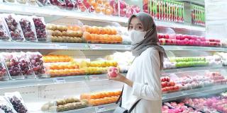 亚洲年轻女子戴着口罩在超市买水果
