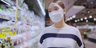 年轻的成年亚洲女性戴着防护口罩，在百货商场精心挑选新鲜产品或消费产品，欢快的新常态购物生活方式。