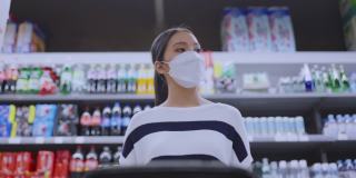 年轻的成年亚洲女性戴着防护口罩，在百货商场精心挑选新鲜产品或消费产品，欢快的新常态购物生活方式。