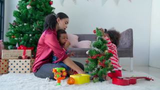 致以节日的问候。亚洲妈妈和非洲裔美国孩子一起庆祝，一起装饰快乐的圣诞树视频素材模板下载