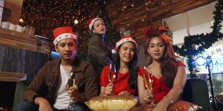 一群亚洲年轻人戴着圣诞帽，在笔记本电脑上与朋友视频通话，庆祝平安夜快乐派对，并碰杯庆祝