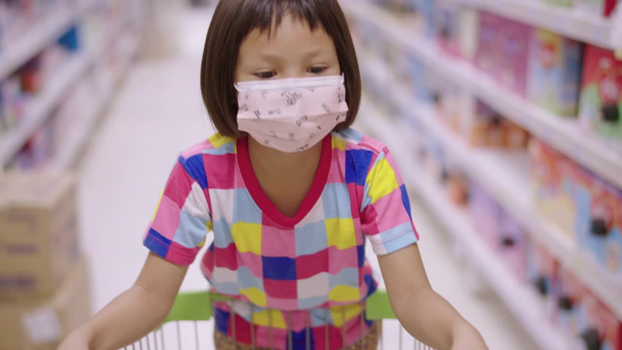 一个亚洲小女孩戴着口罩在当地的超市里走着，看着货架上的产品。