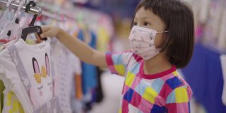 一个亚洲小女孩戴着口罩在当地的超市里走着，看着货架上的产品。