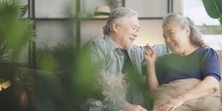 亚洲老老人退休夫妇享受在沙发上谈笑风生，在家里开心地笑着，亚洲老成年人居家隔离期的概念