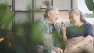 亚洲老老人退休夫妇享受在沙发上谈笑风生，在家里开心地笑着，亚洲老成年人居家隔离期的概念视频素材模板下载