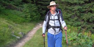 千禧年旅行者的肖像，男游客拿着登山杖和背包从森林中走出来，在山间徒步旅行。旅游的概念。