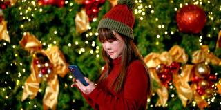 穿着红色毛衣在圣诞树前玩手机的成熟女人