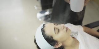 在一家现代沙龙里，一位年轻的女顾客正在用热水蒸脸