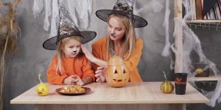 DIY万圣节南瓜。妈妈和女儿穿着女巫服装坐在装饰好的房间里的一张桌子旁。节日装饰。