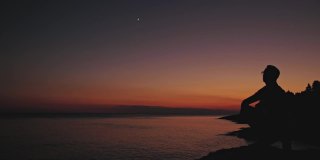 一个人的剪影看着月亮和星星越过海洋的地平线。