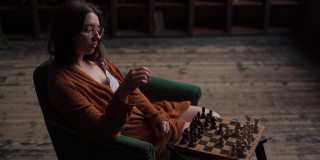 严肃睿智的女棋手戴着眼镜，坐在暗室里下棋走棋。