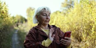 一名身着时尚服装的成熟女性在城市秋季公园用手机视频通话，享受大自然