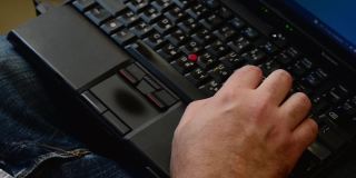 一名男子一边工作一边把手指放在笔记本电脑键盘上