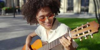 开朗的混血年轻女子卷发弹吉他，在街上唱歌