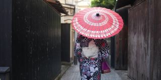 一名日本女子在一条狭窄的小路上行走——撑着纸伞