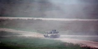 俄罗斯军用坦克在尘土飞扬的道路上行驶，在演习中射击。