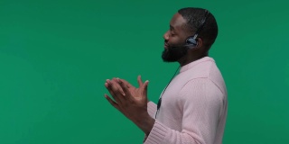 微笑的非裔美国人客户支持男子戴着耳机，对着隔离在绿屏上的麦克风说话，Chroma Key，客户服务代理