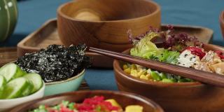 传统的夏威夷美食在餐桌上的特写。煮熟的poke碗与切片蔬菜，鱼和绿叶植物，干海藻。健康的素食。亚洲素食生食，筷子