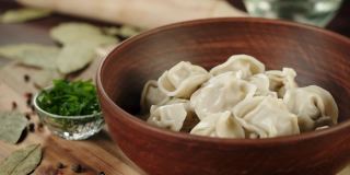 将绿叶小茴香洒在水饺上特写，用肉做面制品。传统的俄罗斯菜。木碗里的乌克兰食物。新鲜的菜